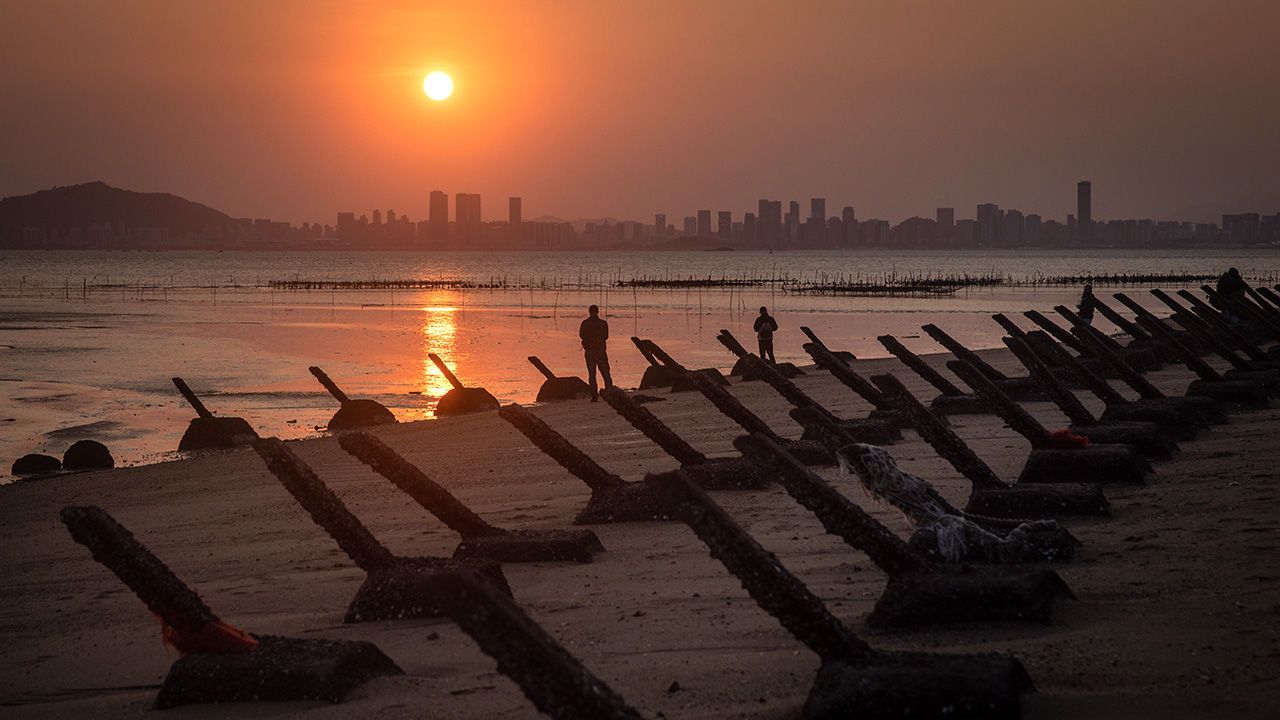 A man, amongst anti-tank fortifications, photographs the sunset over Chinese city Xiamen from Taiwan.