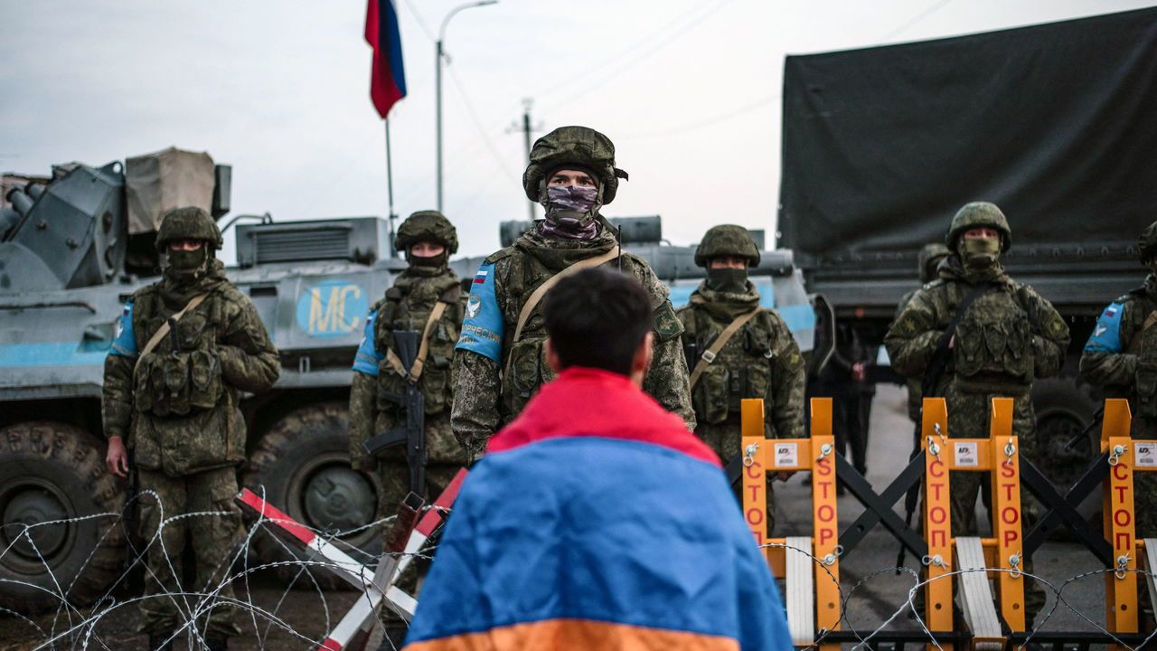 A protester wearing the Armenian national flag stands in front of Russian peacekeepers blocking a road in Nagorno-Karabakh