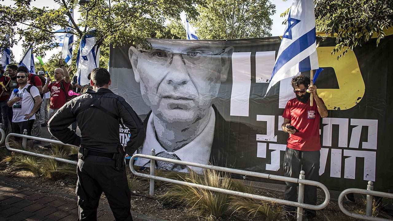 An Israeli police officer stands on guard next to a protest sign showing Israeli minister of Justice Yariv Levin.