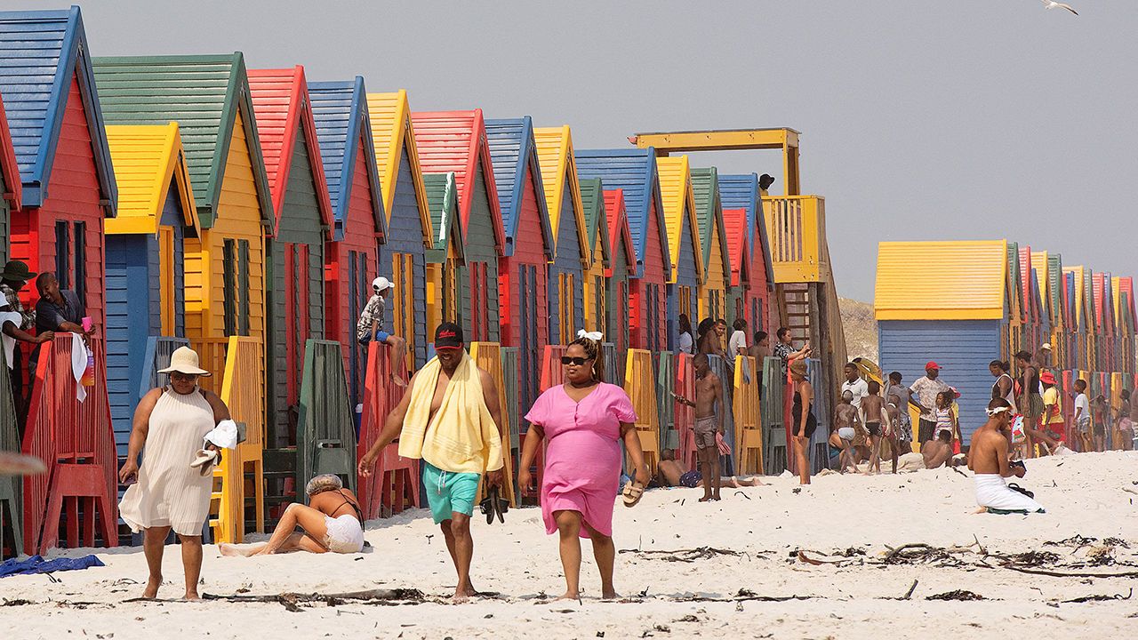 People in front of the colourful bathing huts at Muizenberg Beach, near Cape Town